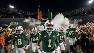 College football team in green and orange uniforms running through a smoke-filled tunnel onto the field at a packed night stadium